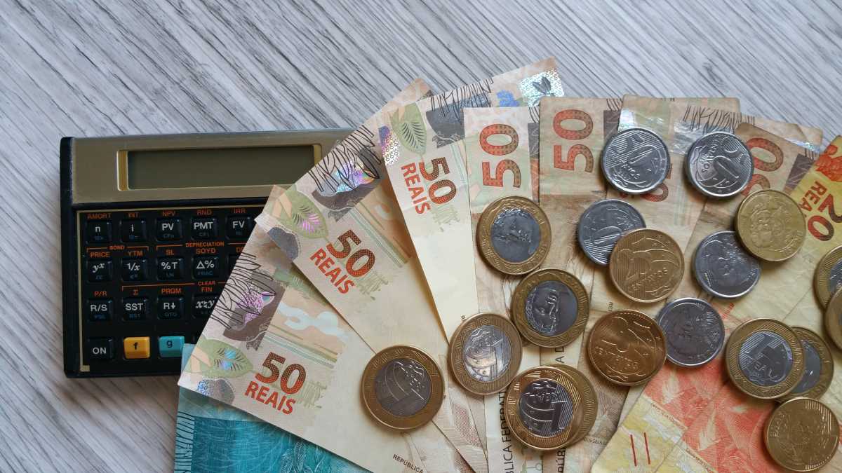 Fotografia colorida mostrando notas e moedas sobre calculadora-Metrópoles