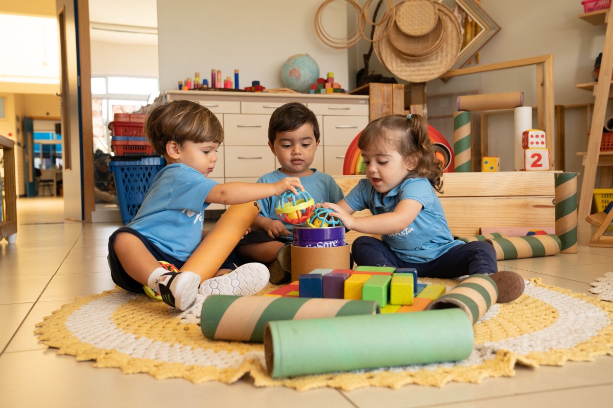 Fotografia colorida mostrando três crianças ao redor de brinquedo educativo-Metrópoles