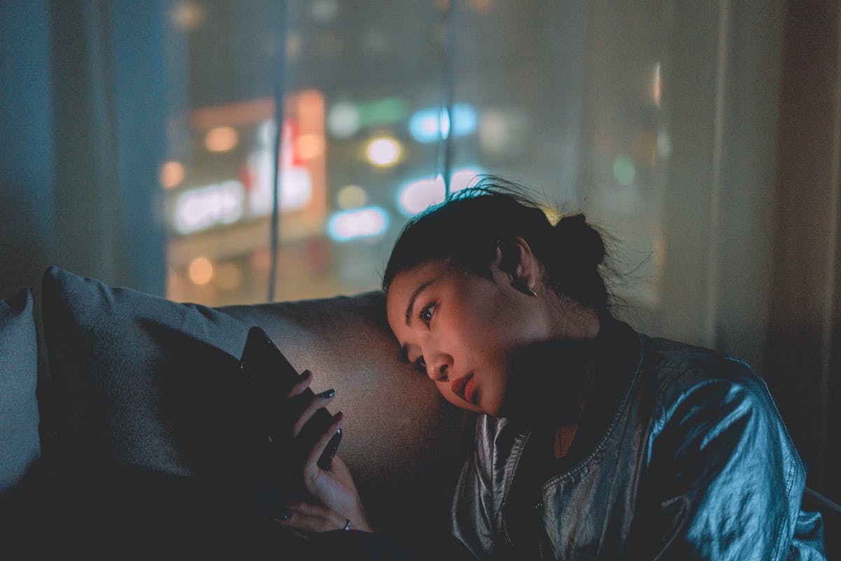 Jovem mulher asiática mexendo em celular no escuro - Metrópoles - ansiedade