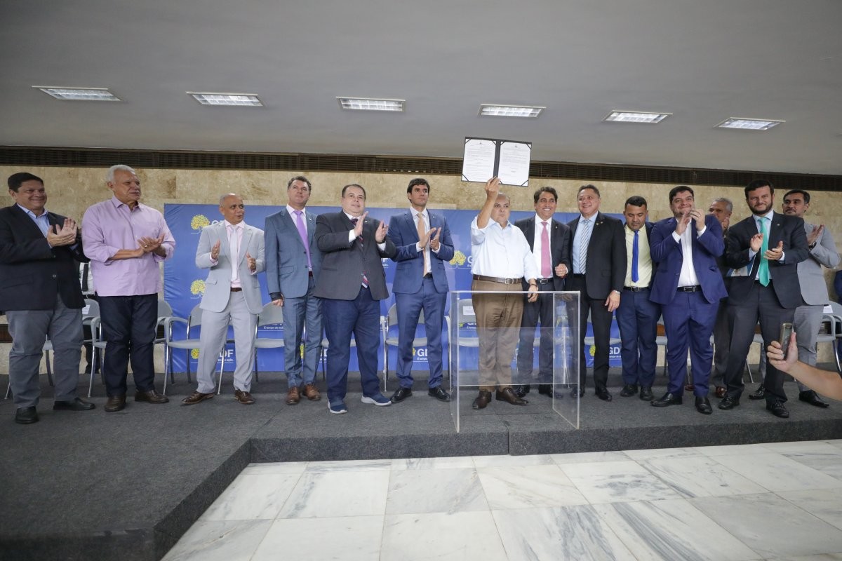 Fotografia colorida mostrando 13 homens em cima de palco durante evento político e o do meio segura um documento em direção ao público-Metrópoles