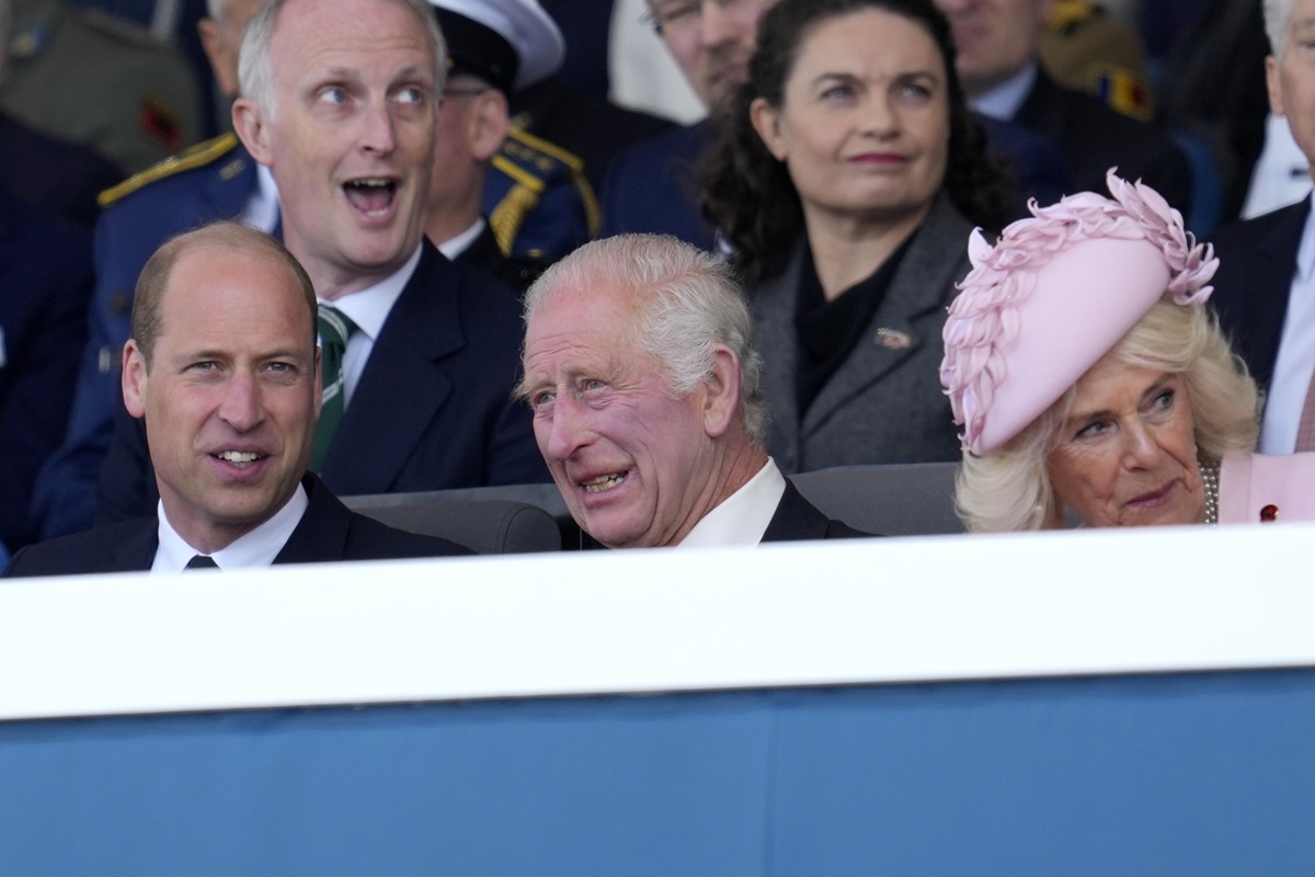 Foto colorida de príncipe William e rei Charles, sendo um idoso, e de uma mulher, rainha Camilla, sentados em uma arquibancada - Metrópoles