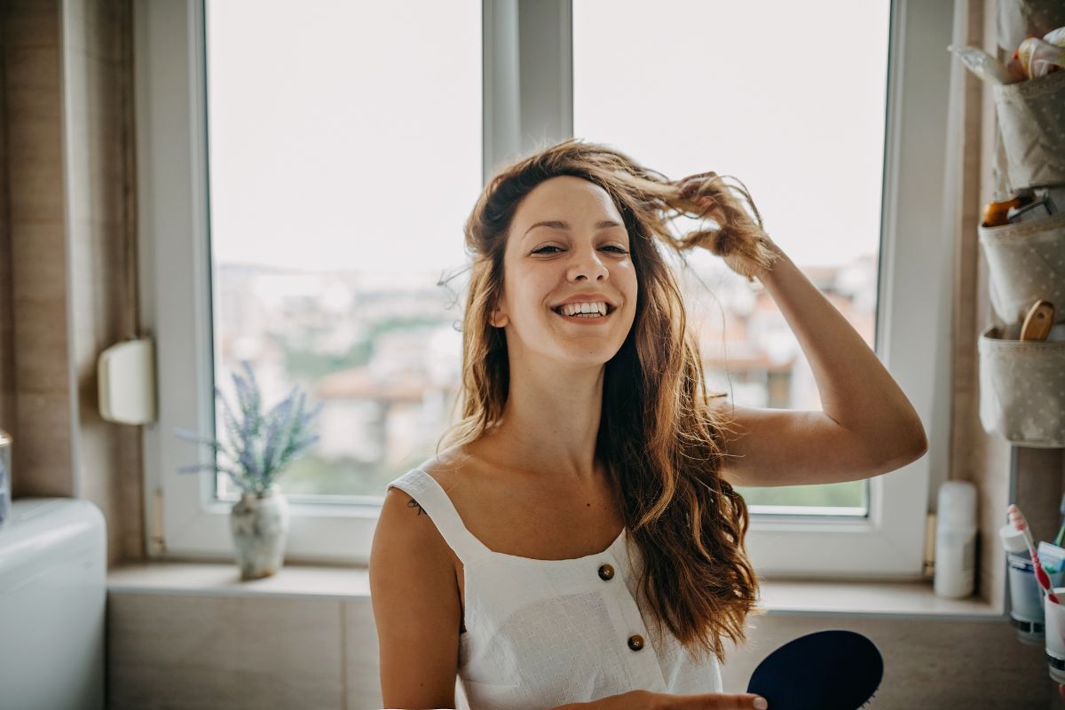 mulher de cabelos longos sorrindo e mexendo no cabelo