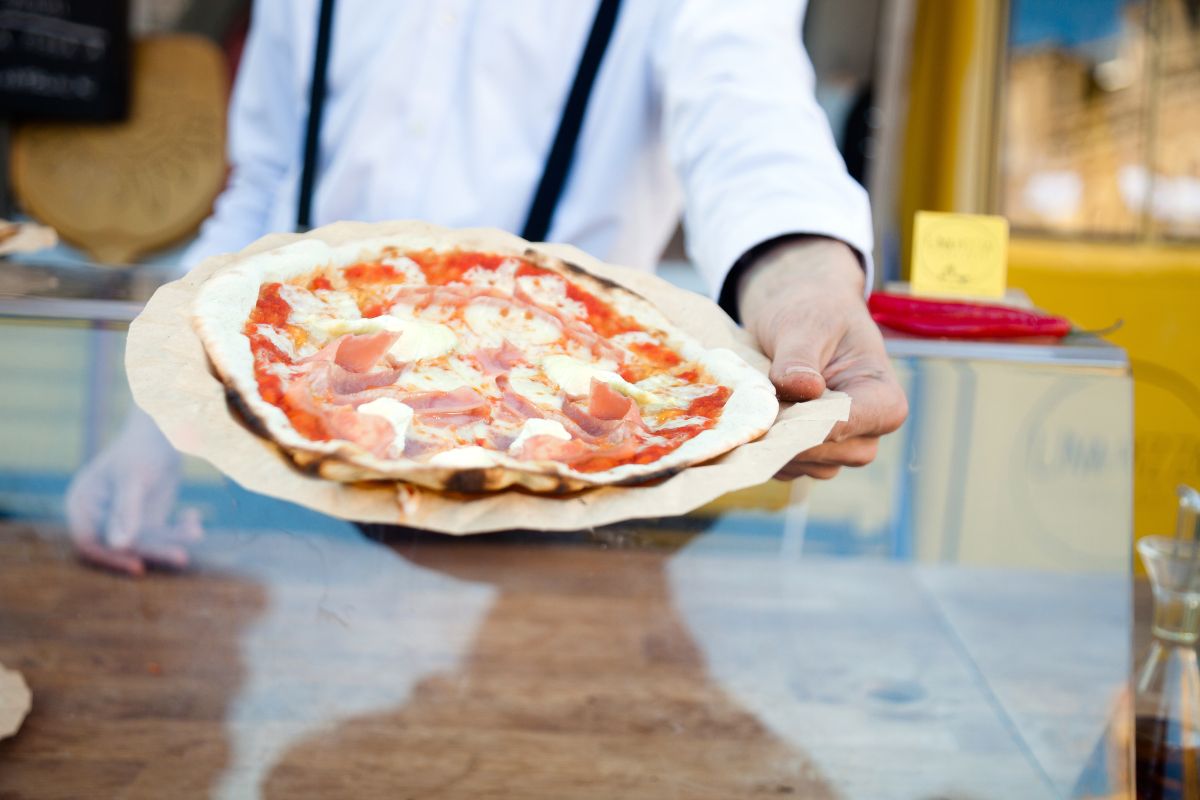 Foto colorida de um homem entregando uma pizza - Metrópoloes - pizzaria