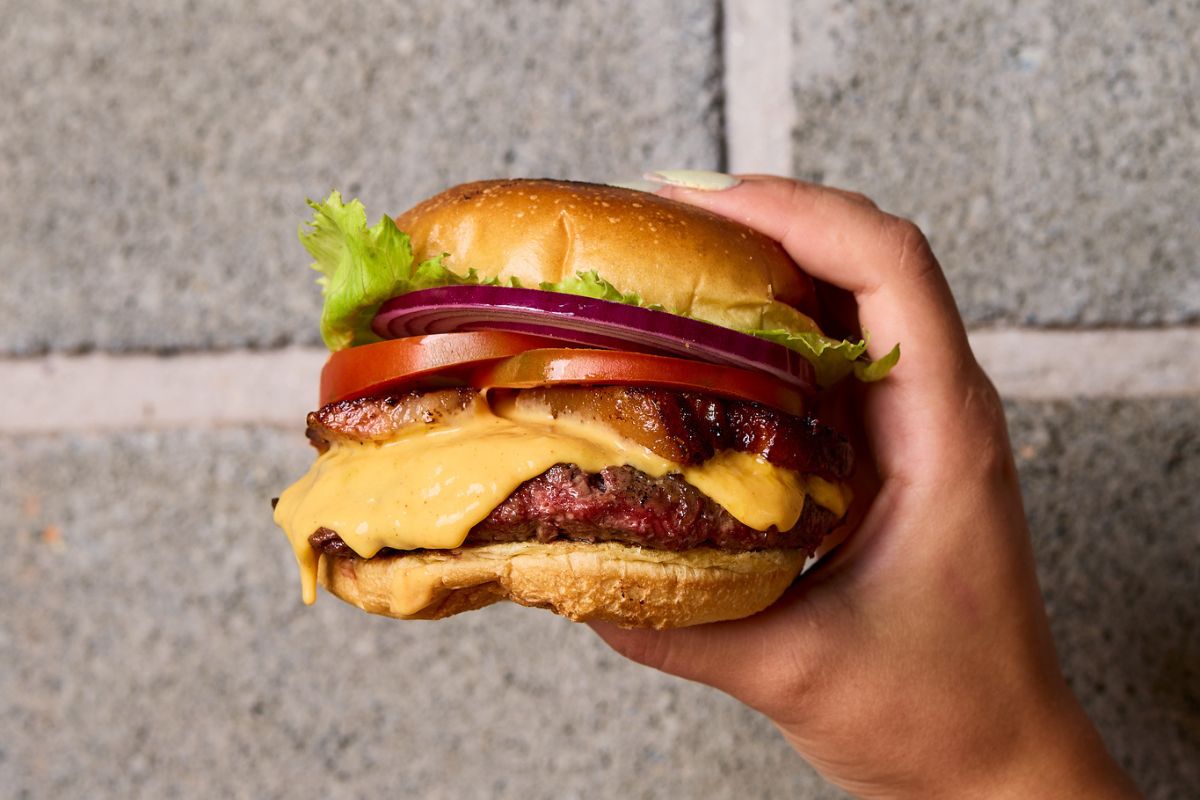 Imagem em close-up de uma mão segurando um hamburguer. Conceito de fast-food, ultraprocessado. Metrópoles