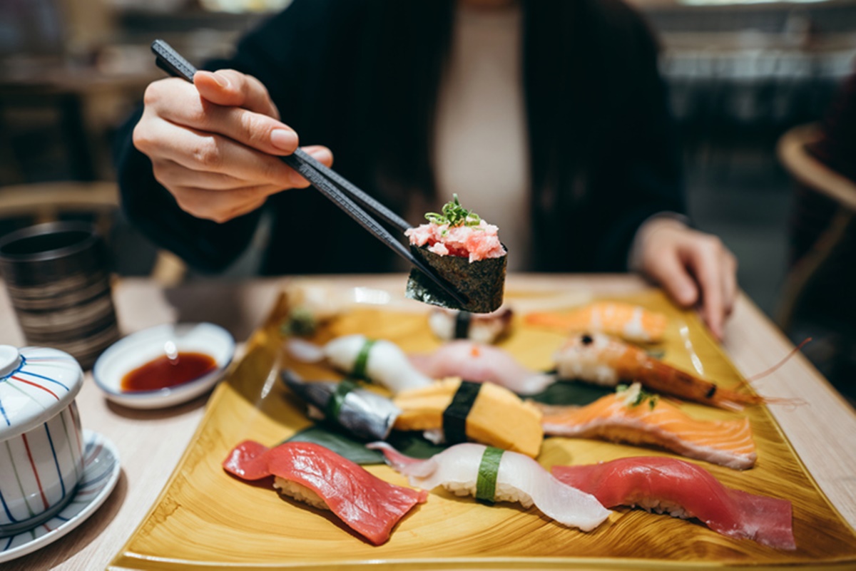 Foto colorida de mulher pegando sushi com hashi - Metrópoles