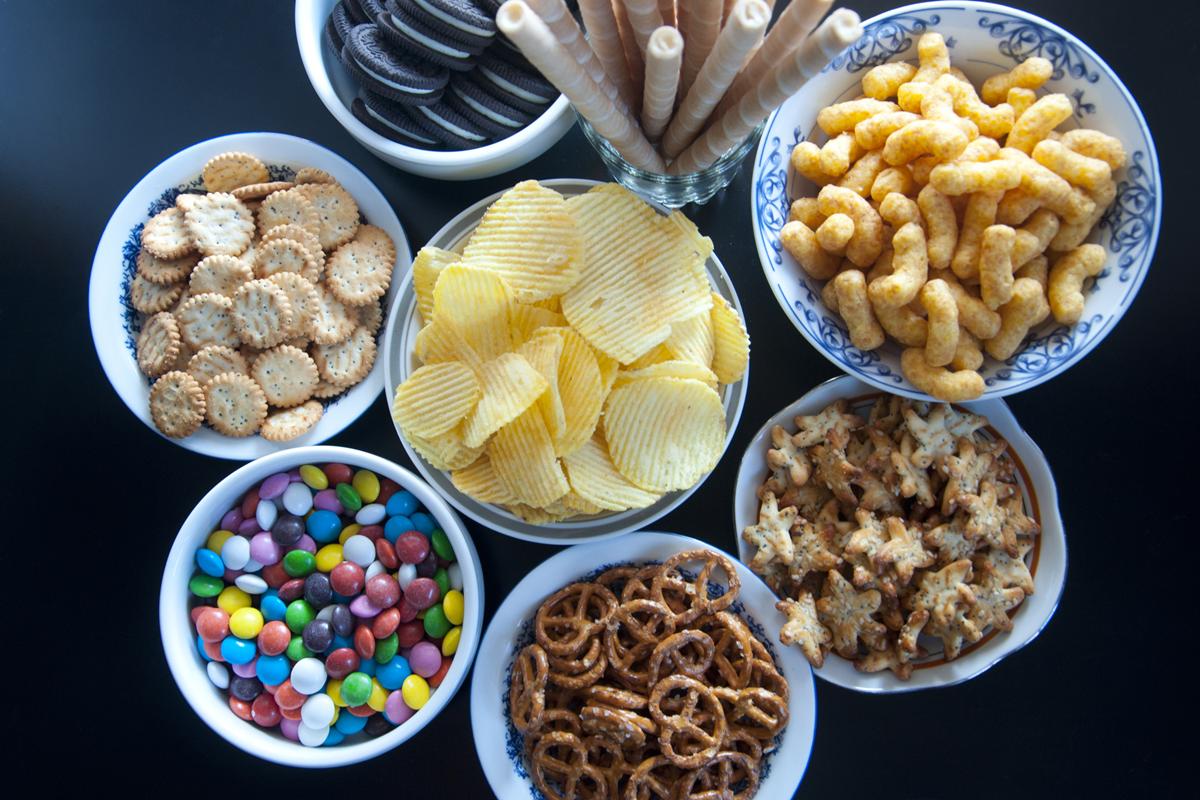 Foto colorida de várias tigelas com balinhas, biscoitos, doces e salgadinhos - Alimentos ultraprocessados, perda de peso