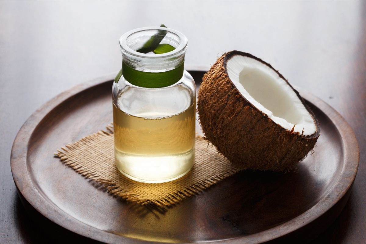 frasco com óleo de coco ao lado de uma metade da fruta