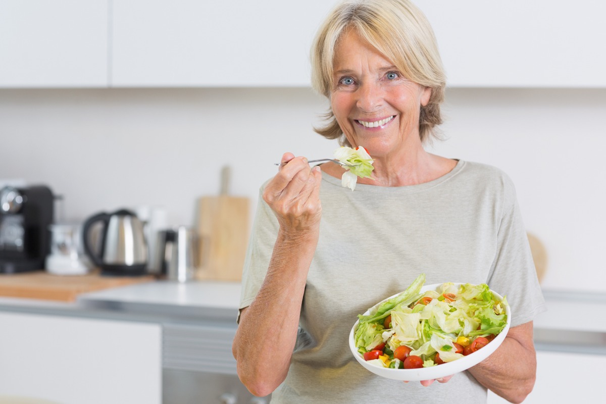 Foto colorida de mulher em cozinha comendo salada - Metrópoles