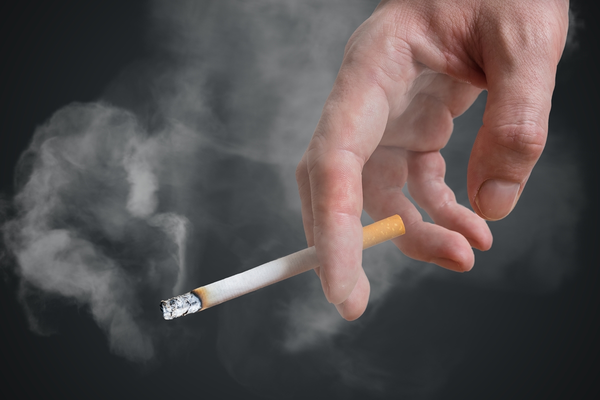 Foto colorida de homem segurando cigarro em fundo preto - Fumante passivo: entenda como a exposição à fumaça prejudica o corpo - Metrópoles
