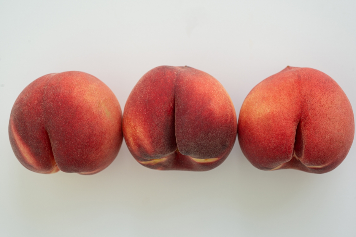 Foto colorida mostra uma fileira de pêssegos sobre uma superfície branca. Imagem faz alusão aos glúteos, bumbum, ânus