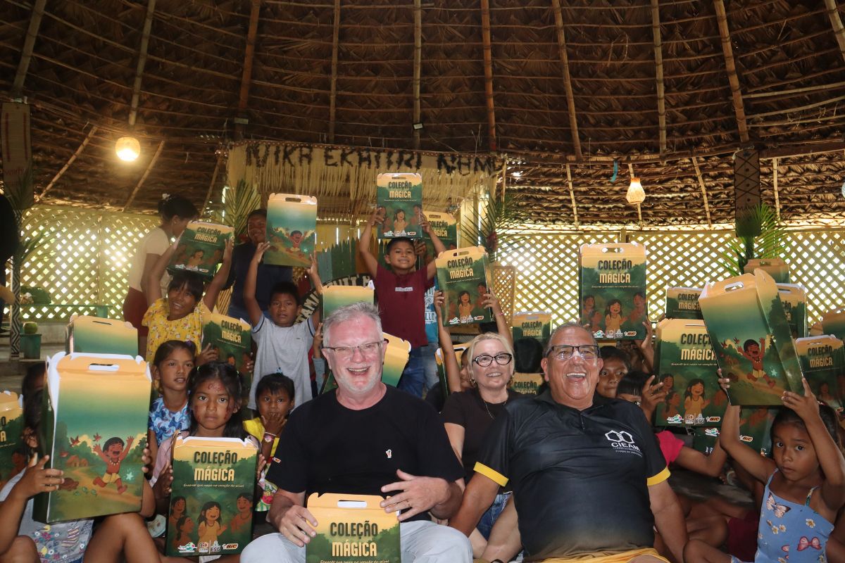 Grupo reunido em ambiente interno, com mesas, caixas e crianças