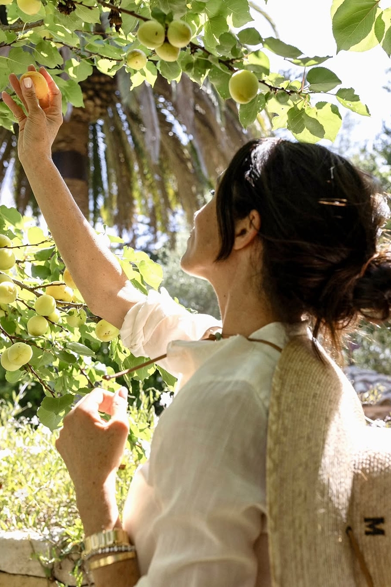 Foto colorida de mulher mexendo em fruto de árvore - Metrópoles