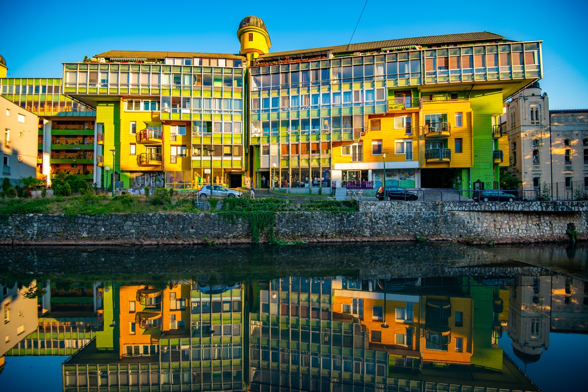 Foto colorida de edifício com paredes coloridas e rio em frente - Metrópoles
