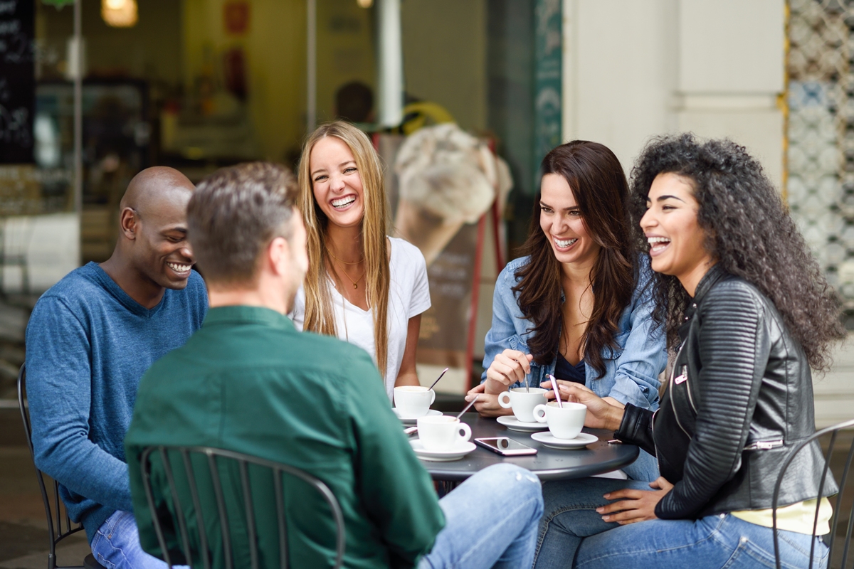 Grupo multirracial de cinco amigos tomando café juntos. Três mulheres e dois homens em uma cafeteria, conversando, rindo e aproveitando o momento. Conceitos de estilo de vida e amizade com pessoas reais. Metrópoles