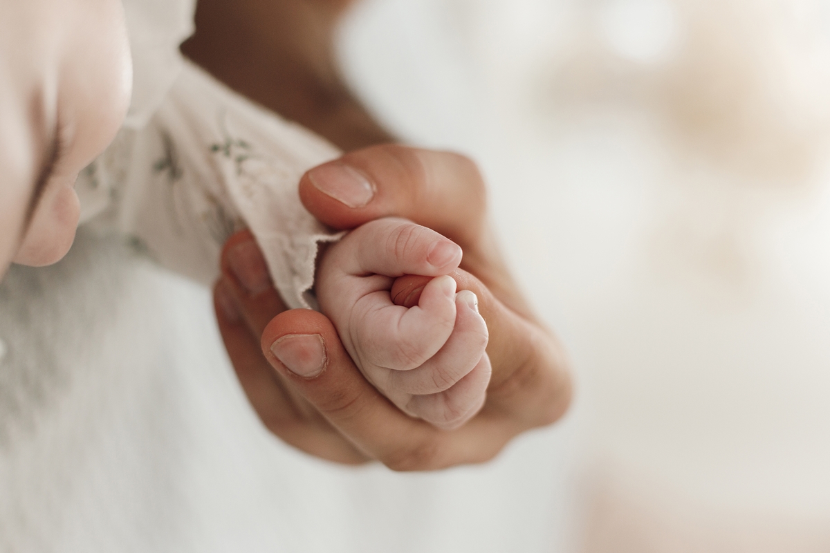 Foto colorida de mãe segurando a mão de um bebê