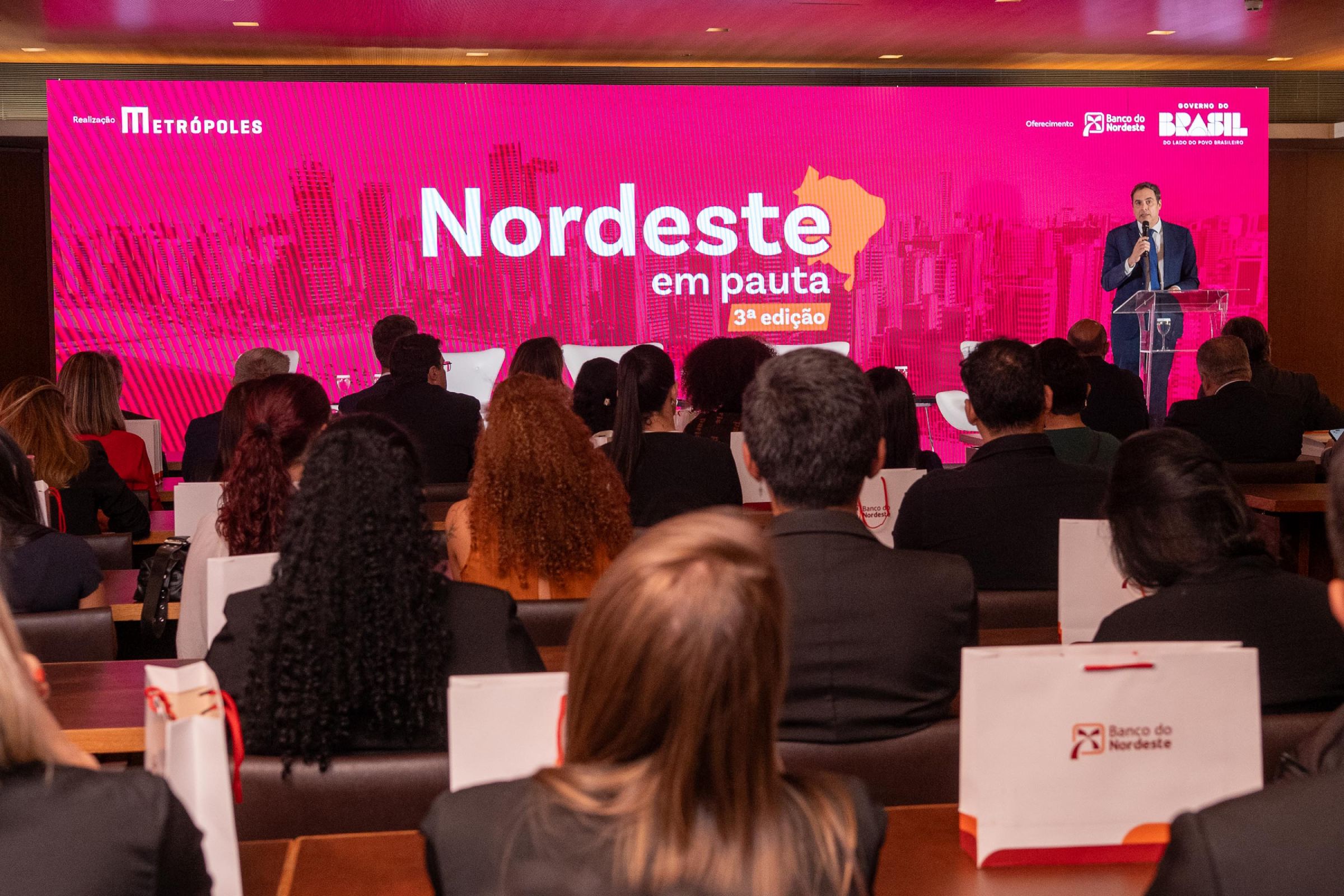 Fotografia colorida mostrando homem de terno discusando em palco-Metróples