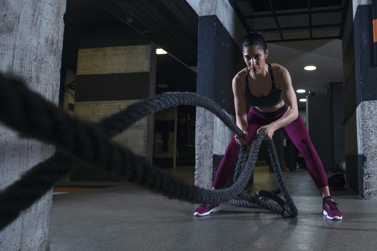Mulher praticando exercícios com cordas navais na academia. Metrópoles