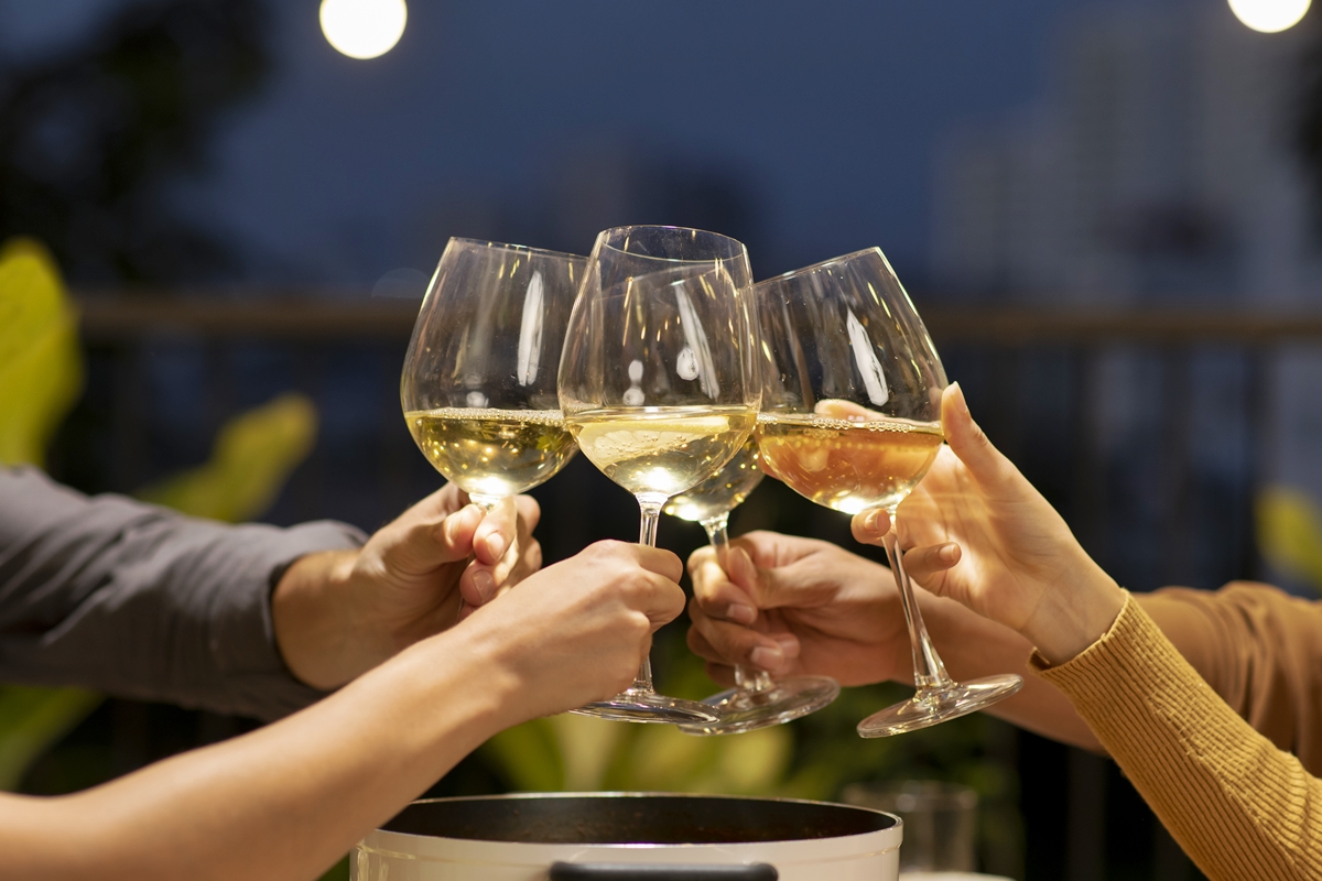 Foto colorida de pessoas brindando com vinho branco