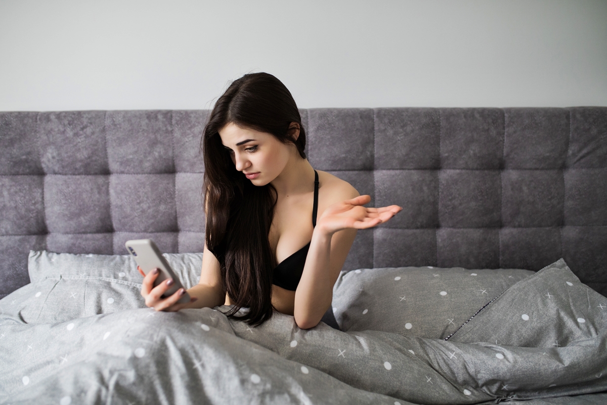 Foto colorida de mulher na cama com o celular