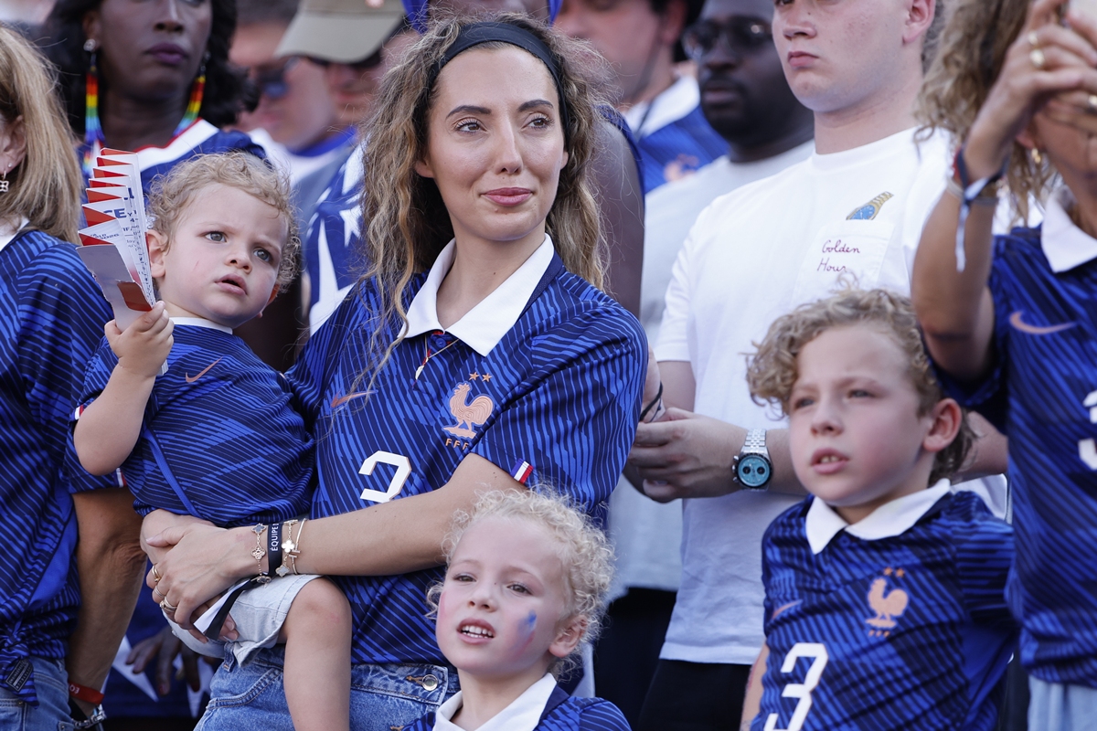 Foto colorida de mulher com três crianças em arquibancada de estádio - Metrópoles