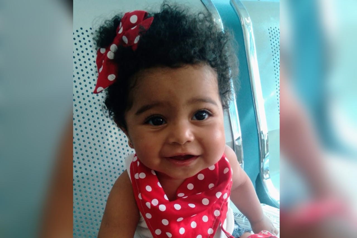 Foto colorida de bebê com adereços vermelhos, sentada, sorrindo para foto - Metrópoles