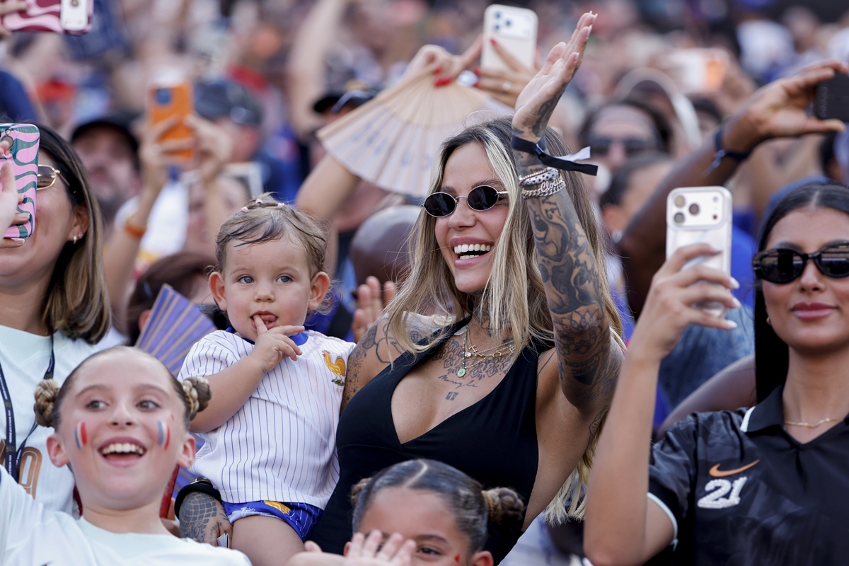 Foto colorida de Zoe Cristofoli com menina no colo em arquibancada de estádio - Metrópoles