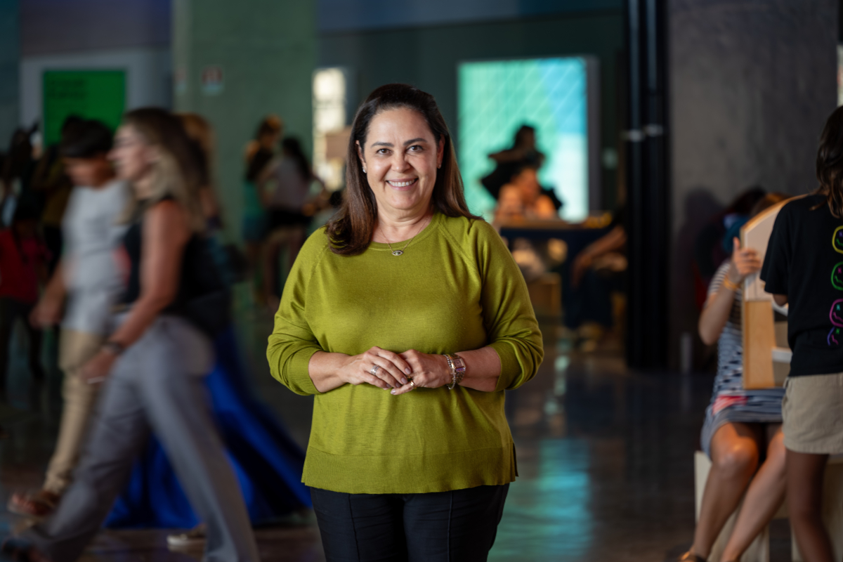 Mulher aparece em pé dentro do espaço do SESI Lab, sorrindo para a câmera.