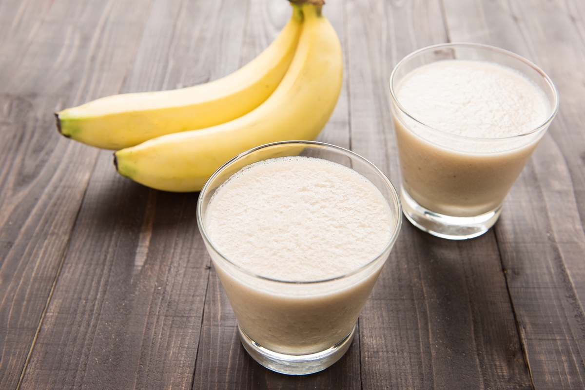 Foto colorida de dois copos de vitamina de banana. Ao fundo, tem uma fruta - Metrópoles
