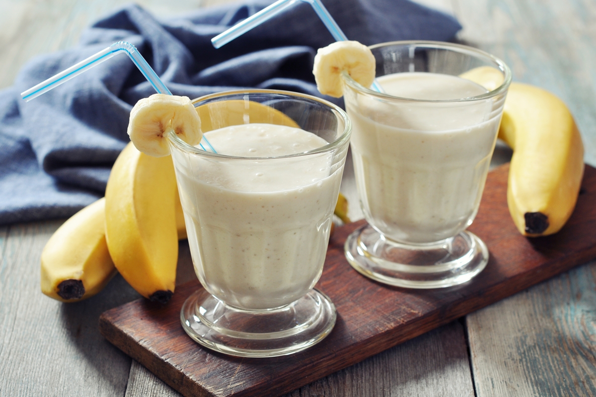 Foto colorida de dois copos de vitamina de banana. Ao fundo, tem uma fruta - Metrópoles