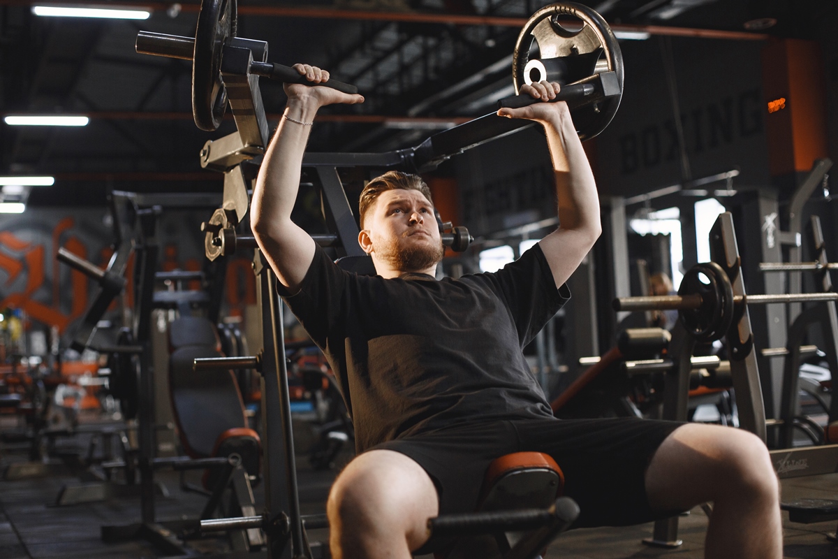 Foto colorida de homem vestido de preto, dentro de uma academia, executando algum exercício direcionado aos membros superiores - Metrópoles.
