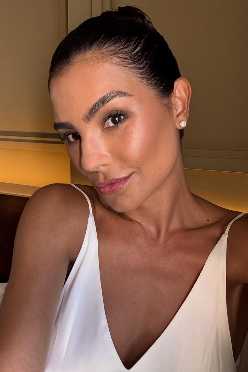 Foto colorida de mulher com blusa branca. Ela está fazendo uma selfie - Metrópoles