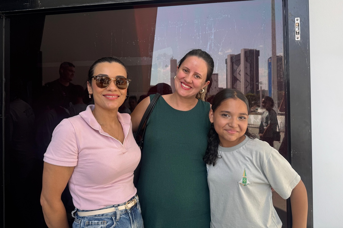 Mulher de blusa rosa, ao lado de outra mulher de blusa verde e uma criança com uniforme da escola - Metrópoles