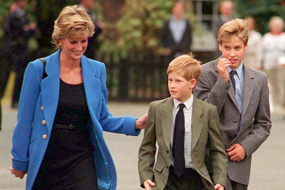 Foto colorida de mulher com blazer azul e vestido preto ao lado de dois garotos com blazer cinza - Metrópoles