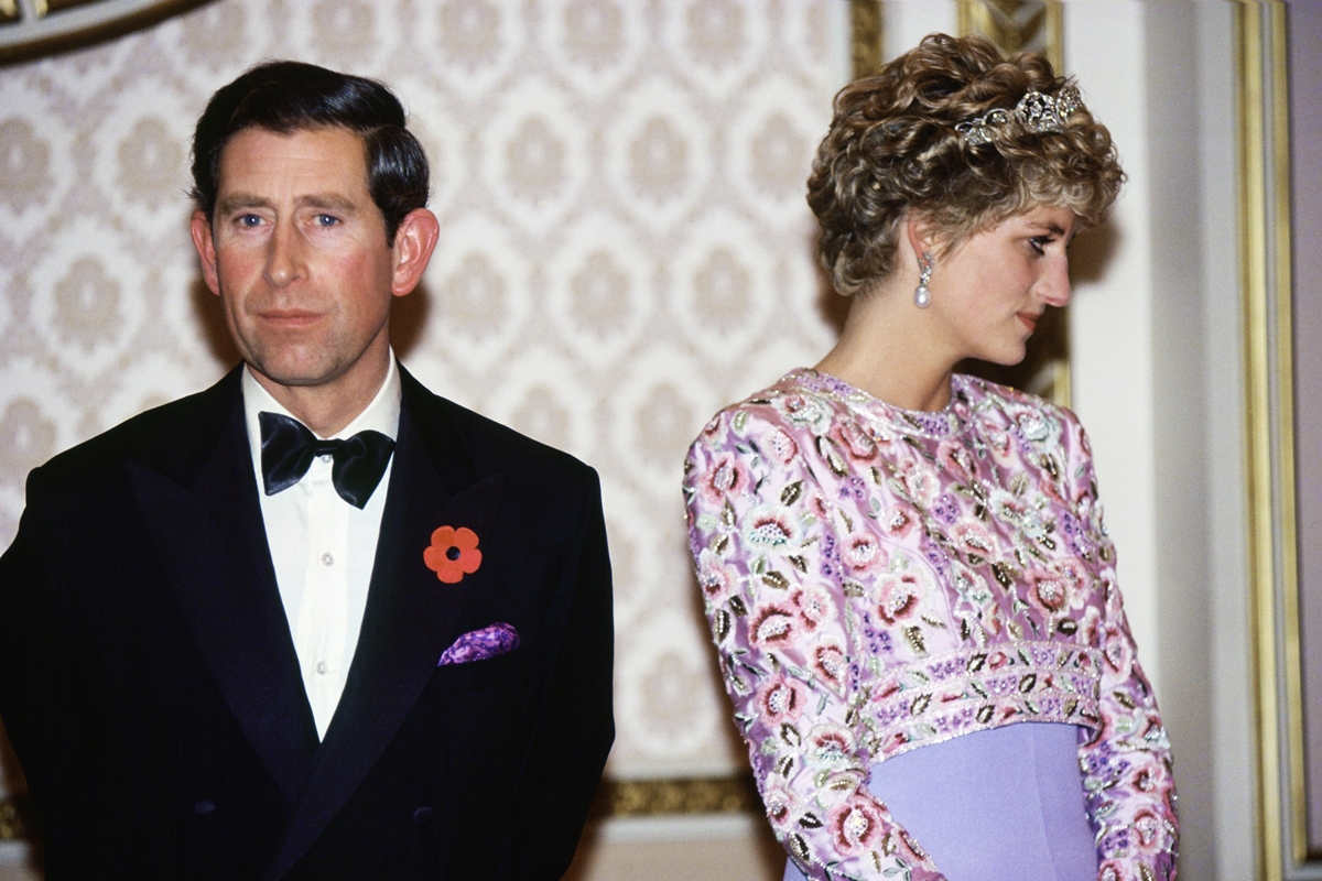 Foto colorida de homem de terno e gravata na cor preta. Ele está ao lado de mulher com roupa na cor lavanda - Metrópoles