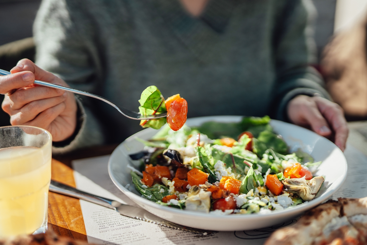 Foto colorida de prato de salada e mão de mulher segurando um garfo - Metrópoles