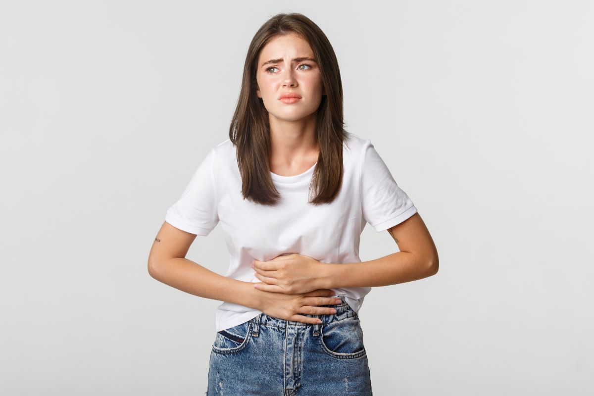 Mulher leva as mãos a barriga com inchaço abdominal - Metrópoles