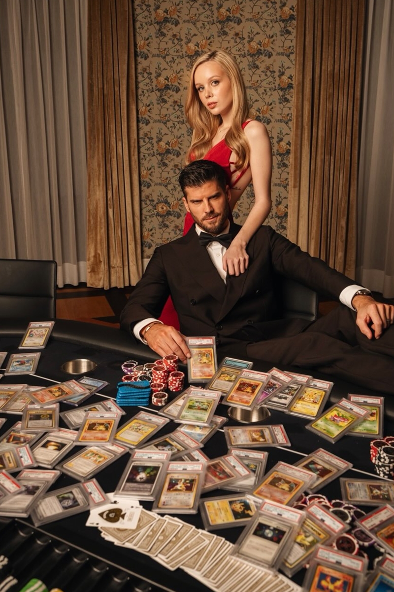 Foto colorida de homem e mulher próximo a uma mesa com cartas Pokémon - Metrópoles